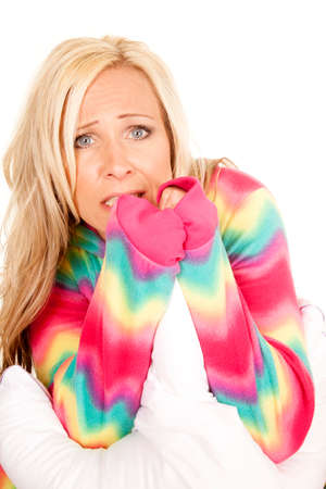 A woman in colorful pajamas with a scared expression on her face holding on to a pillow.の写真素材