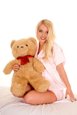 a woman sitting on her bed in her pajamas holding on to her teddy bear.の写真素材