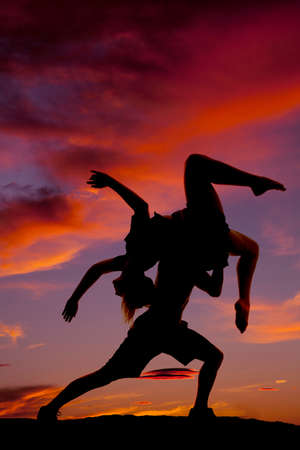 A silhouette of a woman and man dancing in the outdoors, he is lifting her up.の写真素材
