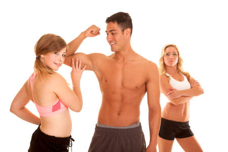 a woman touching her mans muscle while a woman in the background is unhappyの写真素材