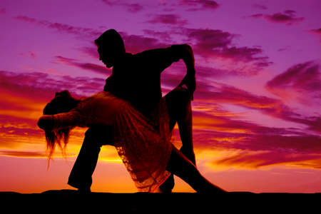 A silhouette of a man and woman dancing she is leaning back over his knee.の写真素材