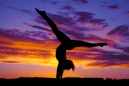 A silhouette of a woman doing a handstand split in the outdoors.の写真素材