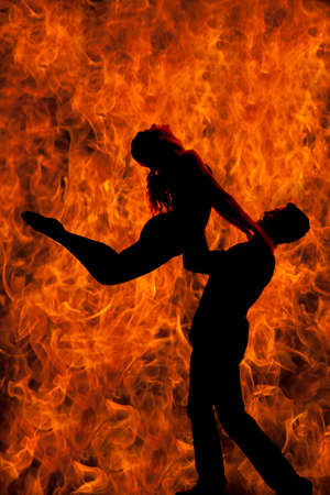 A silhouette of a man and woman dancing, he is doing a lift, with a background of fire.の写真素材