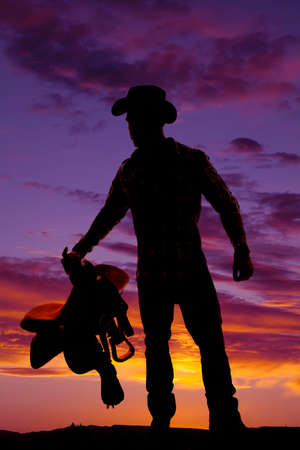 A silhouette of a cowboy in the outdoors, holding on to his saddle.の写真素材
