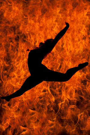 a silhouette of a woman doing a leap with fire behind her.の写真素材