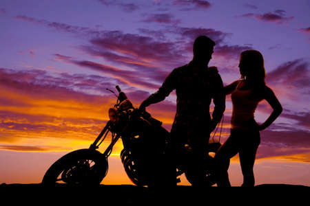 A silhouette of a man on his motorbike with his woman close by.の写真素材