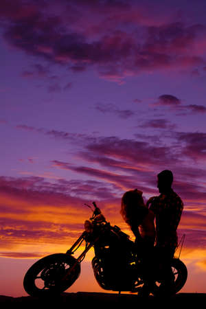 A silhouette of a woman sitting on a motorbike leaning back while her man holds her.の写真素材