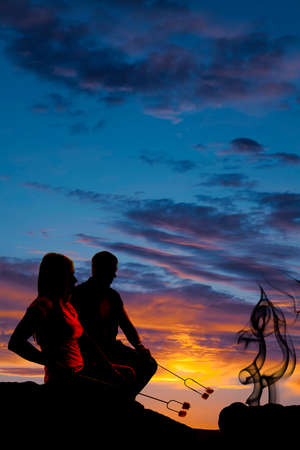 a silhouette of a couple in the outdoors roasting marshmallows.の写真素材
