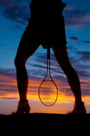 A silhouette of a woman's legs, holding onto a tennis racket.の写真素材