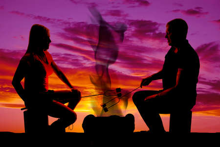 A silhouette of a man and woman in the outdoors, roasting marshmallows.の写真素材