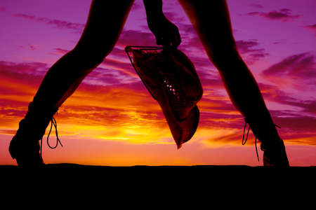A silhouette of a woman's legs holding onto a western cowgirl hat.の写真素材