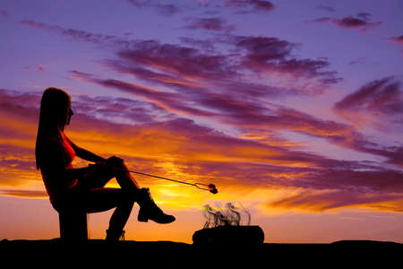 A silhouette of a woman sitting in the outdoors, with a fire roasting a marshmallow.の写真素材