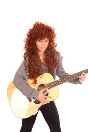 A woman with red curly hair playing her guitar.の写真素材