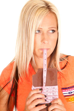 A woman looking to the side with a measuring tape coming out of her mouth, wrapped aroung the candy barの写真素材