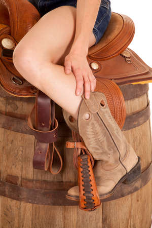A woman sitting on a saddle on a barrel in her cowgirl boots and her short jean shorts.の写真素材