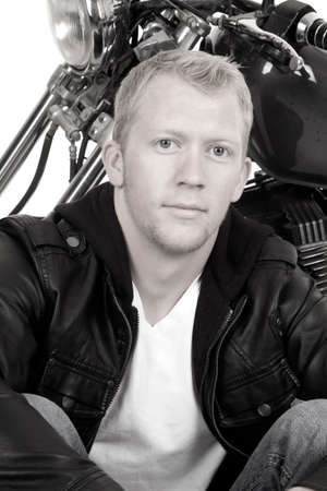A black and white picture of a man sitting in front of his motorcycle looking in his leather jacket.の写真素材