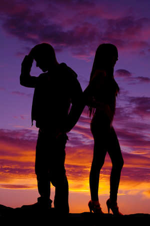 A silhouette of a man and woman back to back in the outdoors.の写真素材