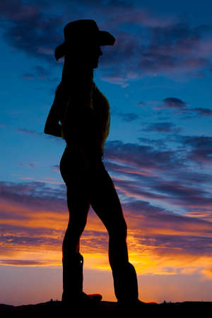 A silhouette of a woman looking to the side with her cowboy hat and boots on.の写真素材
