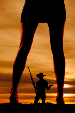 A silhouette of a woman's legs with a cowboy with a rifle and gun in the middle of her legs.の写真素材