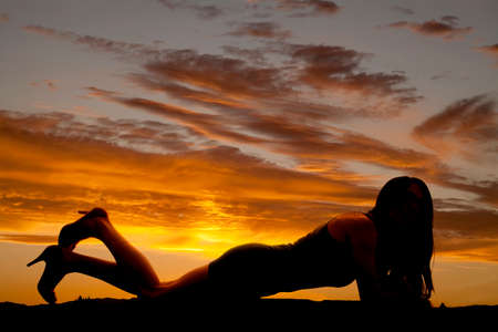 A silhouette of a woman laying down with her high heels kicked up.の写真素材