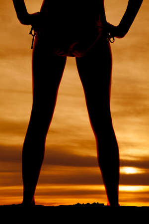 A silhouette of a woman's legs with her hands on her hips, in the outdoors.の写真素材