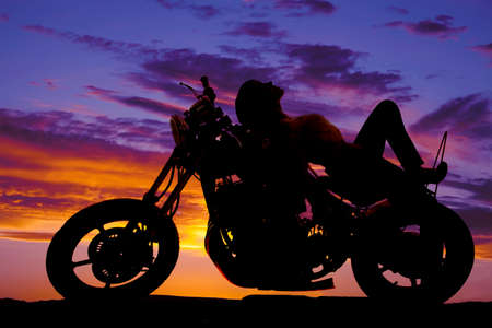 A silhouette of a woman laying back on the back of a motorcycle in the outdoors.の写真素材