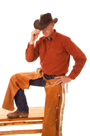 a cowboy with his foot up on a bench, touchin the brim of his hat, looking down.の写真素材