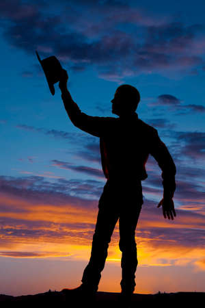 a silhouette of a man holding on to her hat.の写真素材