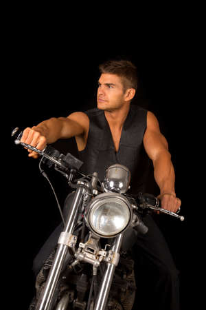 A man in his black vest sitting on his motorcycle looking to the side.の写真素材