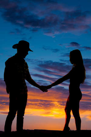 A silhouette of a cowboy holding on to his woman's hand in the outdoors.の写真素材