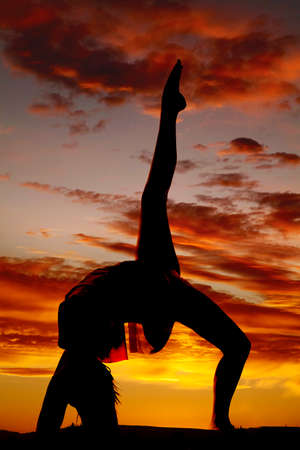 A silhouette of a woman doing a back bend in the outdoors.の写真素材
