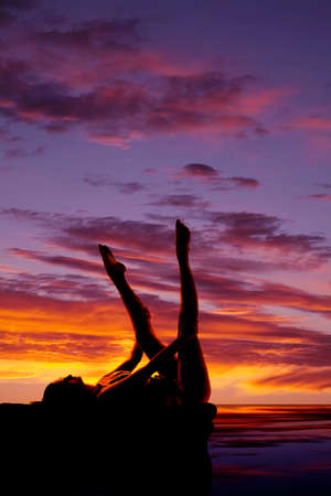 A silhouette of a woman laying on her back holding on to her legs moving.の写真素材