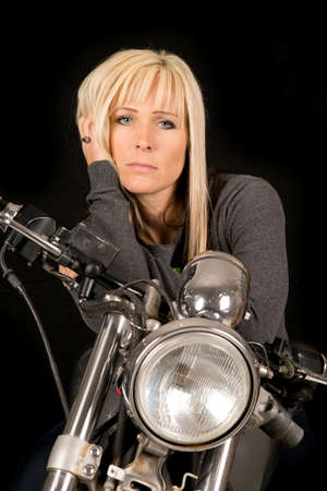 A woman sitting on her motorcycle with her hand in her hair.の写真素材