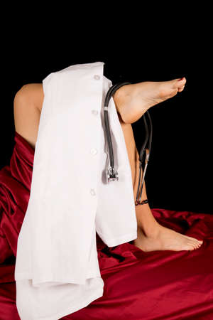 A woman laying in bed with a doctors jacket and a stethoscope on her legs.の写真素材