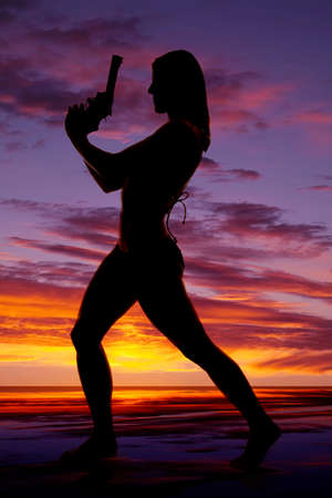 A silhouette of a woman standing with a pistol pointing up.の写真素材