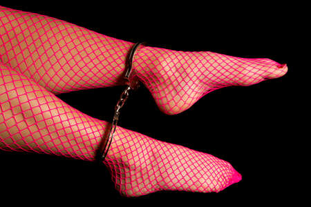 A woman legs in pink fishnet stockings and handcuffs on her ankles.の写真素材