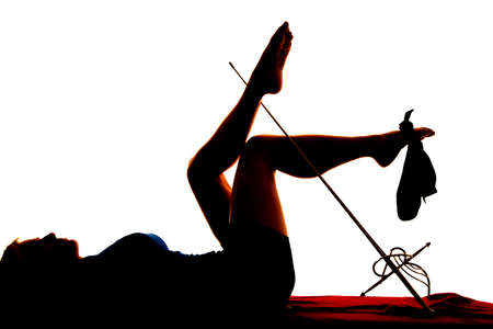 A silhouette of a woman laying on a bed with a sword on her legs and a hat on her foot.の写真素材