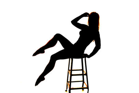A silhouette of a woman balancing herself on a stool.の写真素材