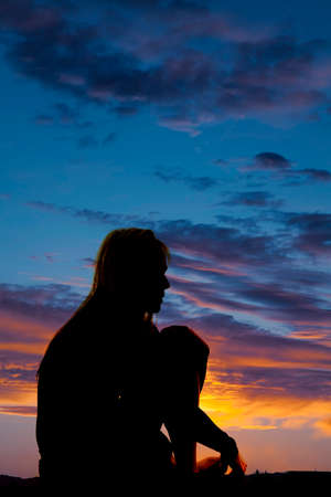 a silhouette of a woman sitting down in the outdoors, curled up thinking.の写真素材