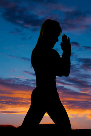 a silhouette of a woman kneeling in the outdoors praying.の写真素材