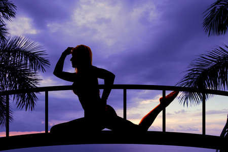 A silhouette of a woman in the outdoors on a bridge stretchingの写真素材