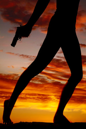 A silhouette of a woman running with a pistol in her hands.の写真素材