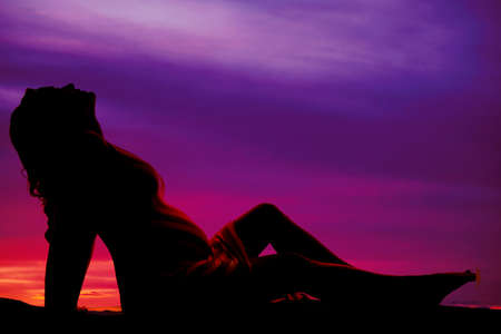 A silhouette of a woman sitting on the ground looking upの写真素材