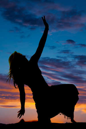 A silhouette of a woman kneeling in her skirt posing.の写真素材