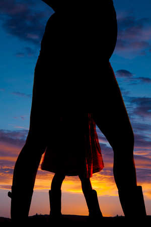 a silhouette of a pregnant woman in her western boots, with a little girls legs between hers.の写真素材