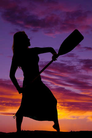 A silhouette of a woman holding on to a paddle in the outdoors.の写真素材