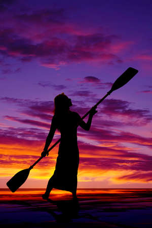 a silhouette of a woman on vacation with her paddles in her hands.の写真素材