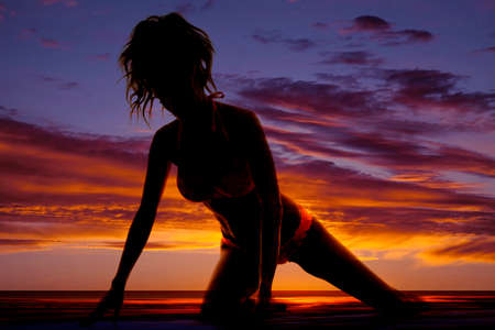A silhouette of a woma kneeling in the outdoors in her bikini.の写真素材