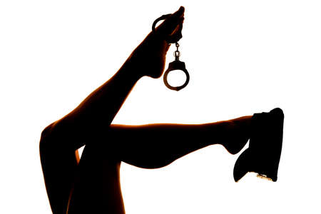 A silhouette of a woman's legs with a police hat on and cuffs on her toes.の写真素材