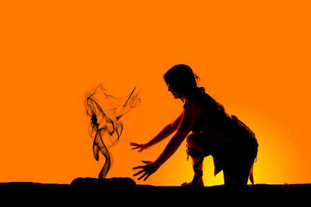 A silhouette of a cave woman kneeling down by a fire.の写真素材